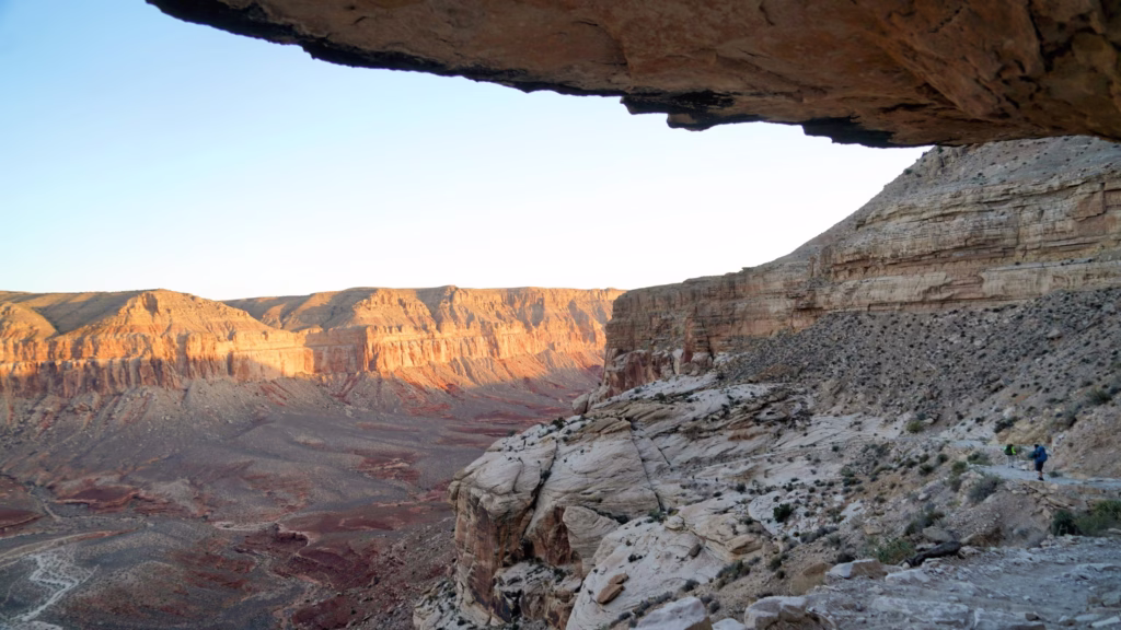 Hikers follow a rocky trail high above the floor of Hualapai Canyon. Sunrise illuminates the top portion of the fall canyon wall.